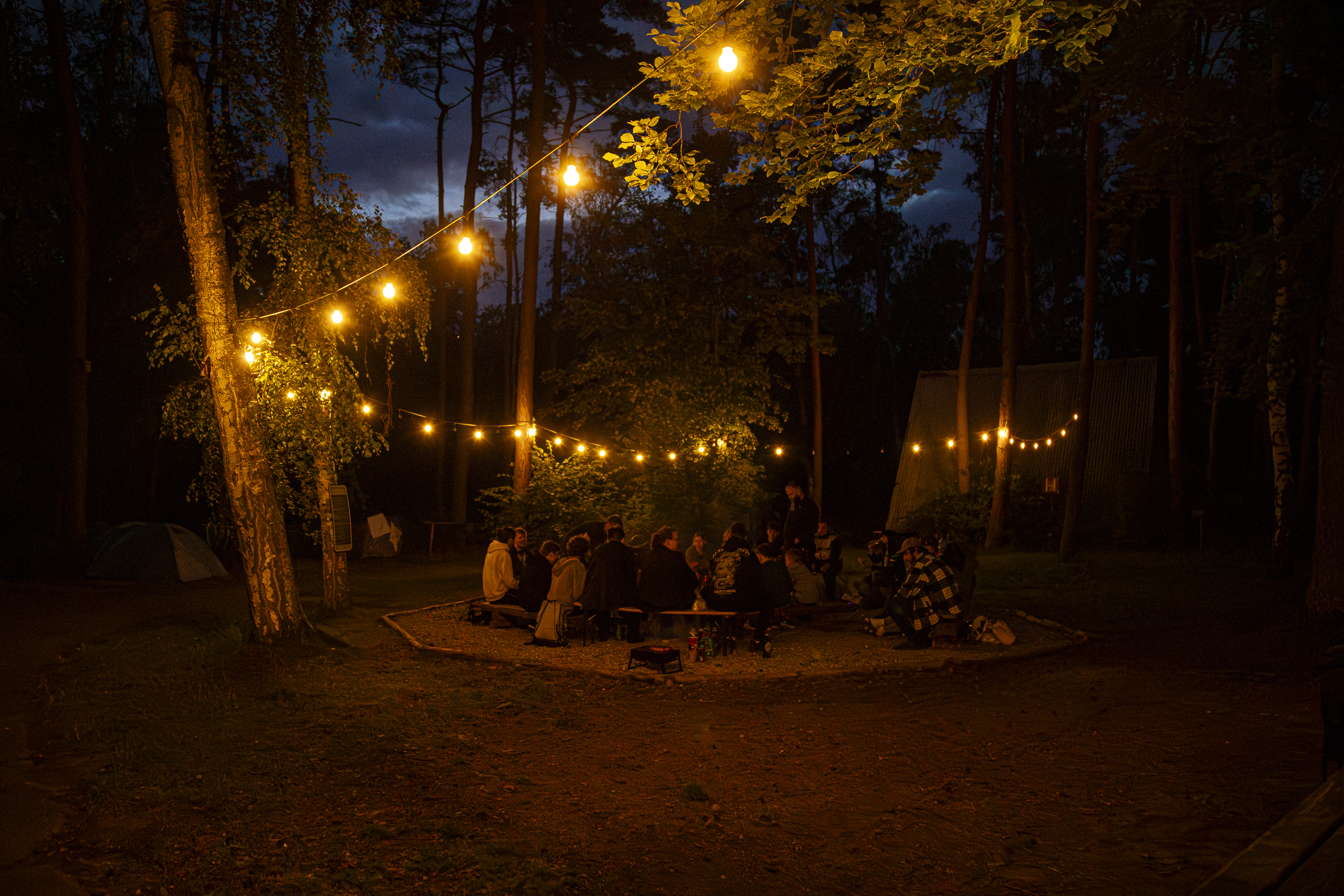 Wieczorne ognisko pod girlandą lampek, ludzie wokół